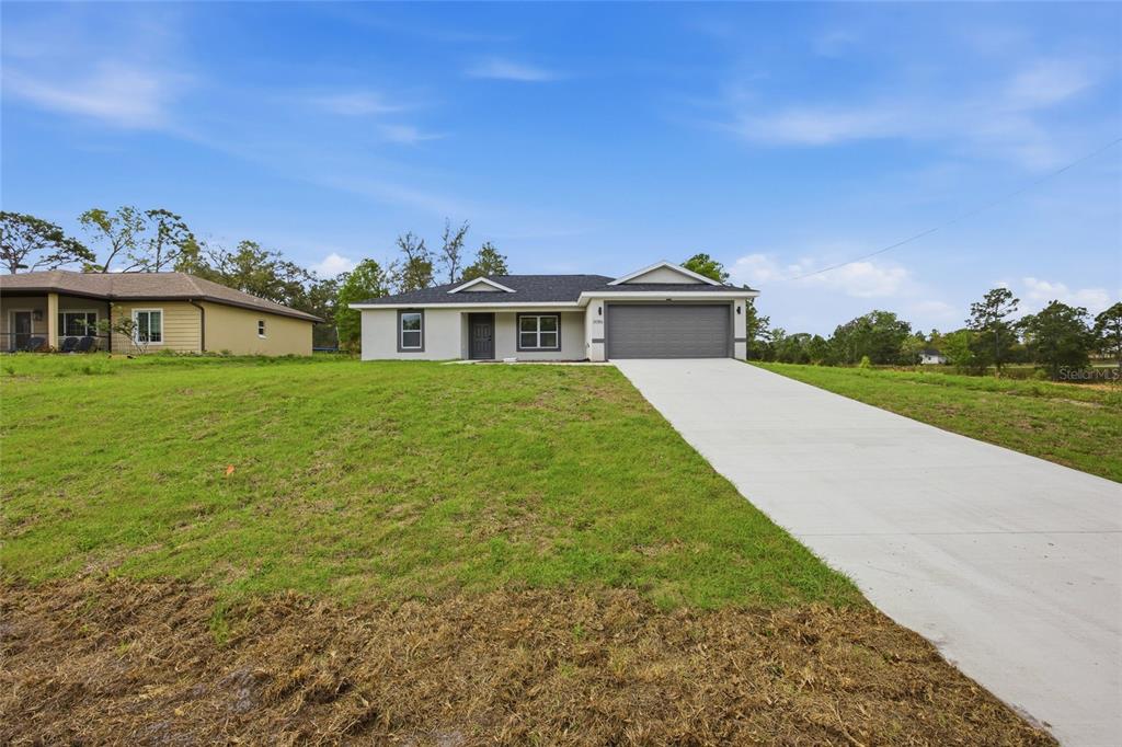 A single-story house with a gray garage and a concrete driveway sits on a lawn — 3086 W HAMPSHIRE BOULEVARD, CITRUS SPRINGS, FL
