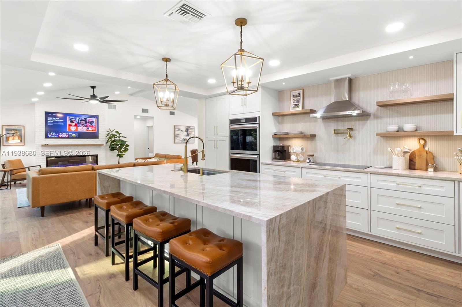 A modern kitchen features a large stone island with leather stools and white cabinetry — 3540 NE 28th Ave, Lighthouse Point FL 33064, LIGHTHOUSE POINT, FL