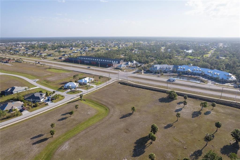 An aerial view shows a large, undeveloped grassy lot adjacent to a multi-lane highway — 16490 TRADING POST ROAD, PUNTA GORDA, FL