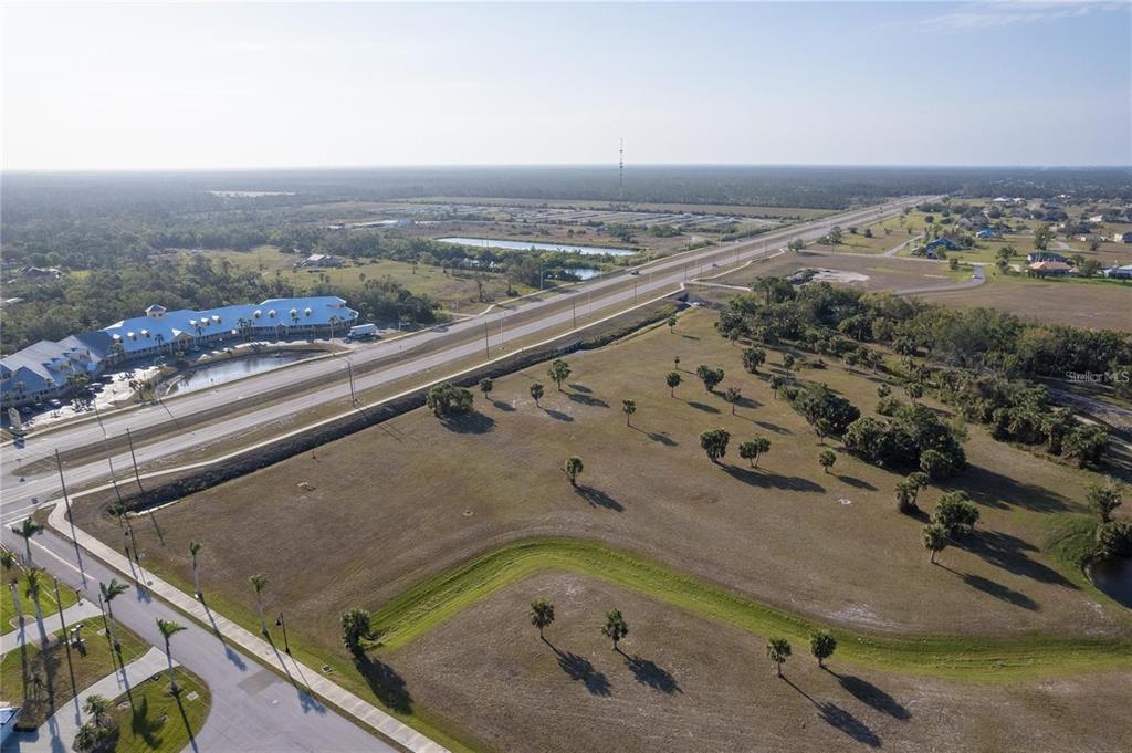 An aerial view shows a large, undeveloped grassy lot next to a multi-lane highway — 16490 TRADING POST ROAD, PUNTA GORDA, FL