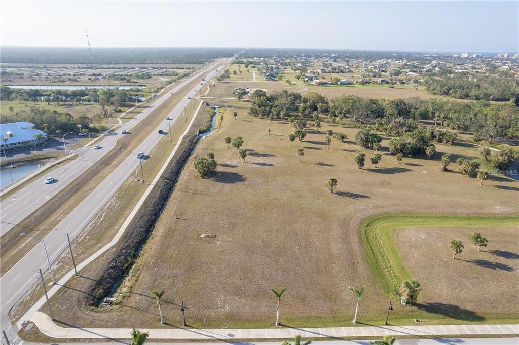 An aerial view shows a large, vacant grassy lot adjacent to a multi-lane highway — 16490 TRADING POST ROAD, PUNTA GORDA, FL
