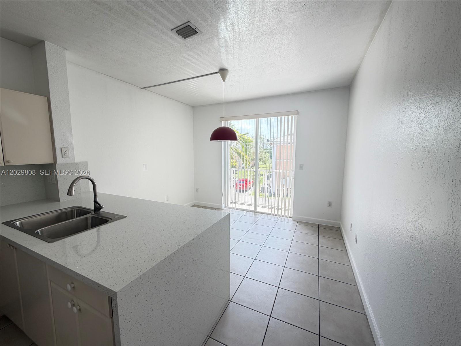 A kitchen with a quartz island, double sink, and dining area leading to a sliding door — 7080 NW 177th St # 13, Hialeah FL 33015, HIALEAH, FL