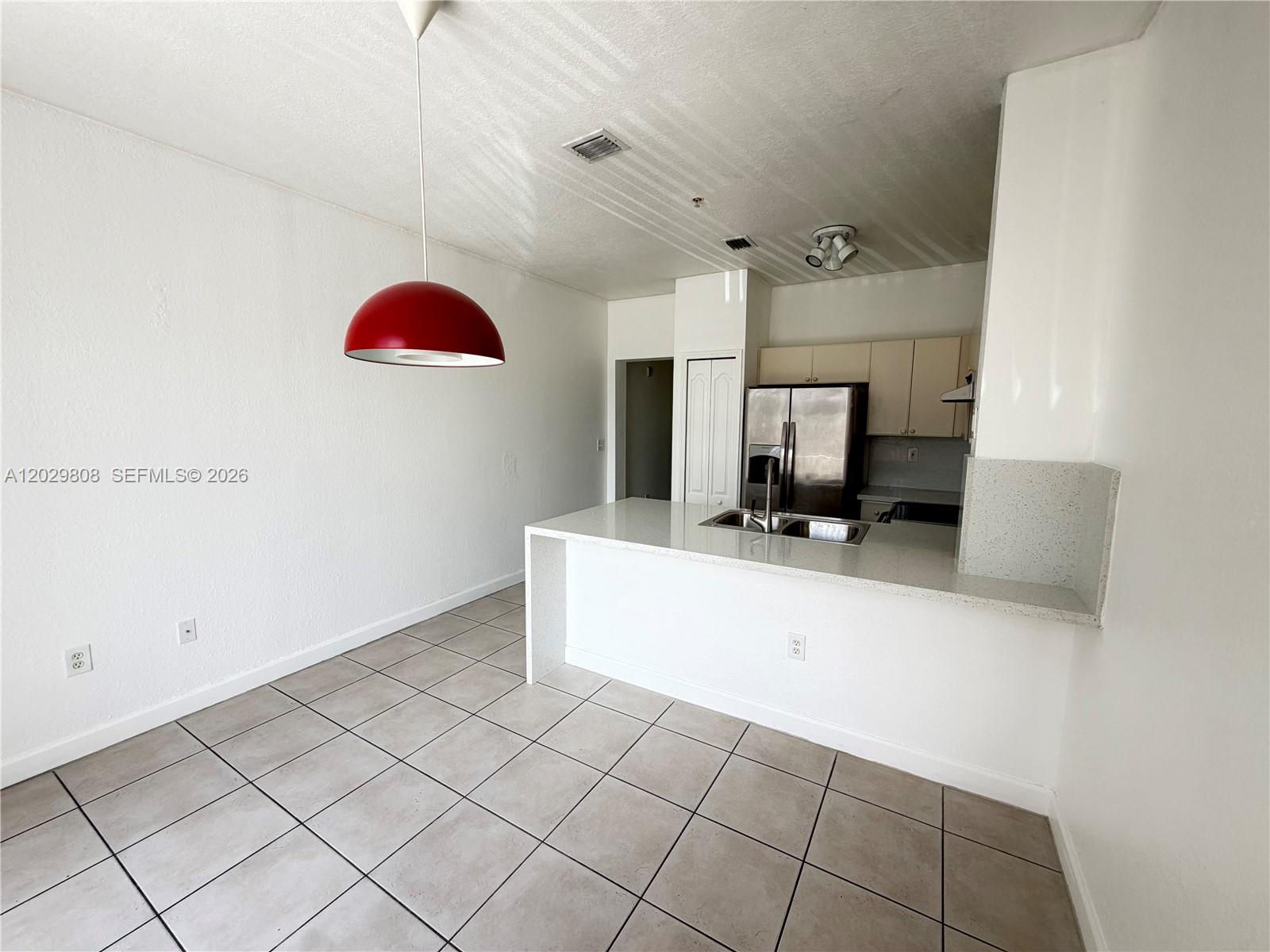 A kitchen with a breakfast bar, stainless steel refrigerator, and a red pendant light fixture — 7080 NW 177th St # 13, Hialeah FL 33015, HIALEAH, FL
