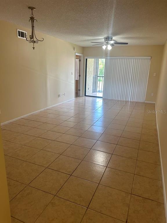 An empty room with tan tile flooring, a ceiling fan, and a sliding glass door — 3245 CANDLE RIDGE DRIVE UNIT 203, ORLANDO, FL
