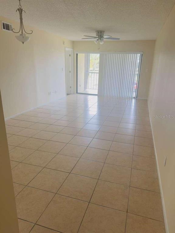 An empty living room features beige tile flooring, a ceiling fan, and sliding glass balcony doors — 3245 CANDLE RIDGE DRIVE UNIT 203, ORLANDO, FL