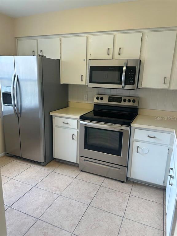 A kitchen features white cabinets, stainless steel appliances, and light-colored tile flooring — 3245 CANDLE RIDGE DRIVE UNIT 203, ORLANDO, FL