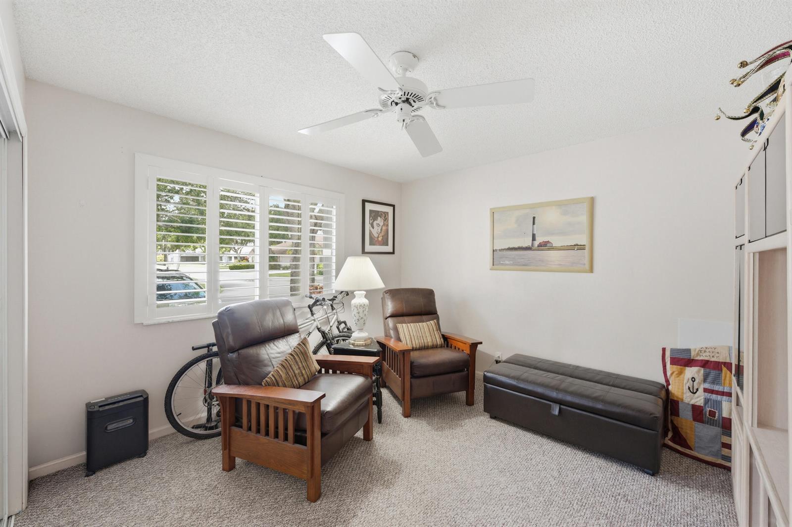 A carpeted room features two leather armchairs, a storage ottoman, a ceiling fan, and shutters — 180 Par Drive, Royal Palm Beach FL 33411, ROYAL PALM BEACH, FL