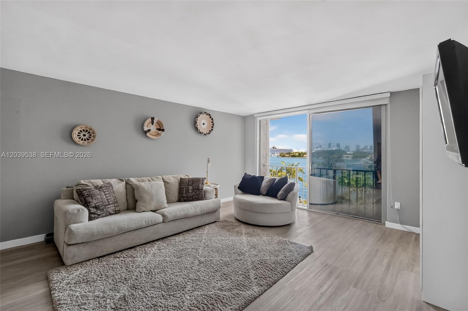 A living room features a beige sofa, round chair, gray walls, and a waterfront balcony view — 800 West Ave # 533, Miami Beach FL 33139, MIAMI BEACH, FL