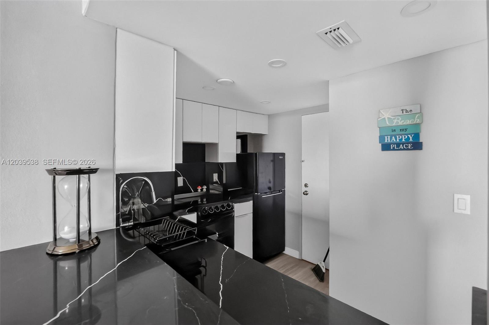 A kitchen features black countertops, white cabinetry, and a black refrigerator against a white wall — 800 West Ave # 533, Miami Beach FL 33139, MIAMI BEACH, FL