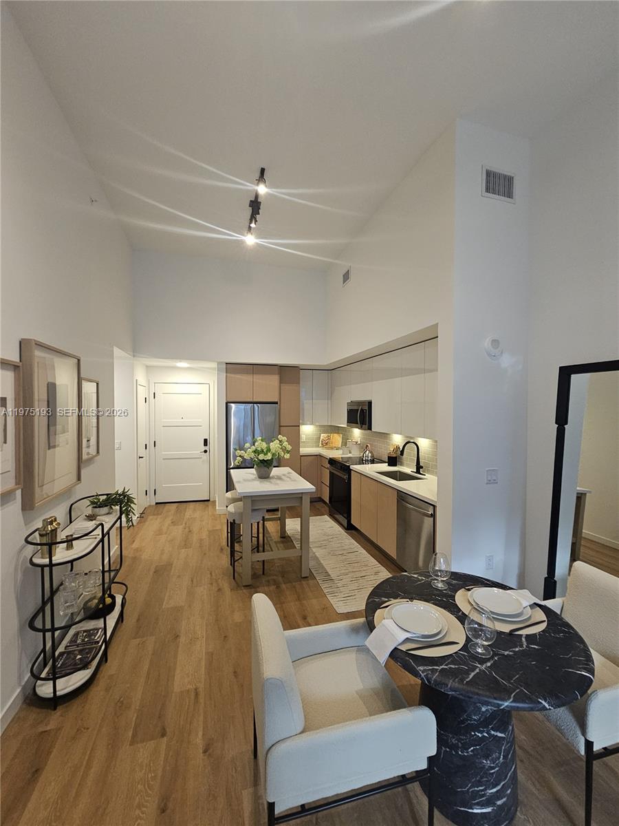 A modern kitchen with light wood cabinets and a marble-topped island opens into a dining area — 1650 NE 124th St # 102, North Miami FL 33181, NORTH MIAMI, FL