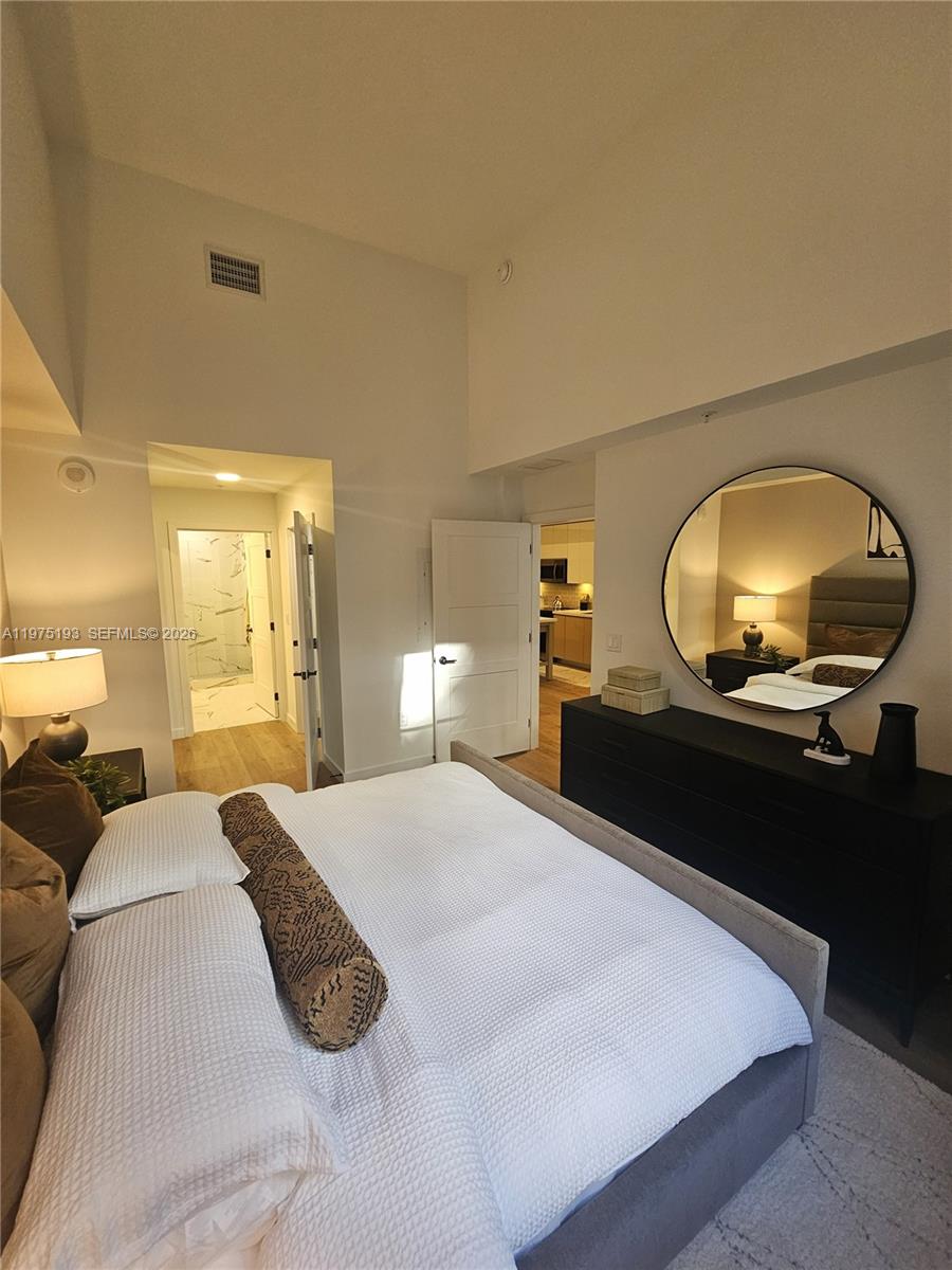 A bedroom features a bed, a round mirror above a dresser, and two doorways — 1650 NE 124th St # 102, North Miami FL 33181, NORTH MIAMI, FL