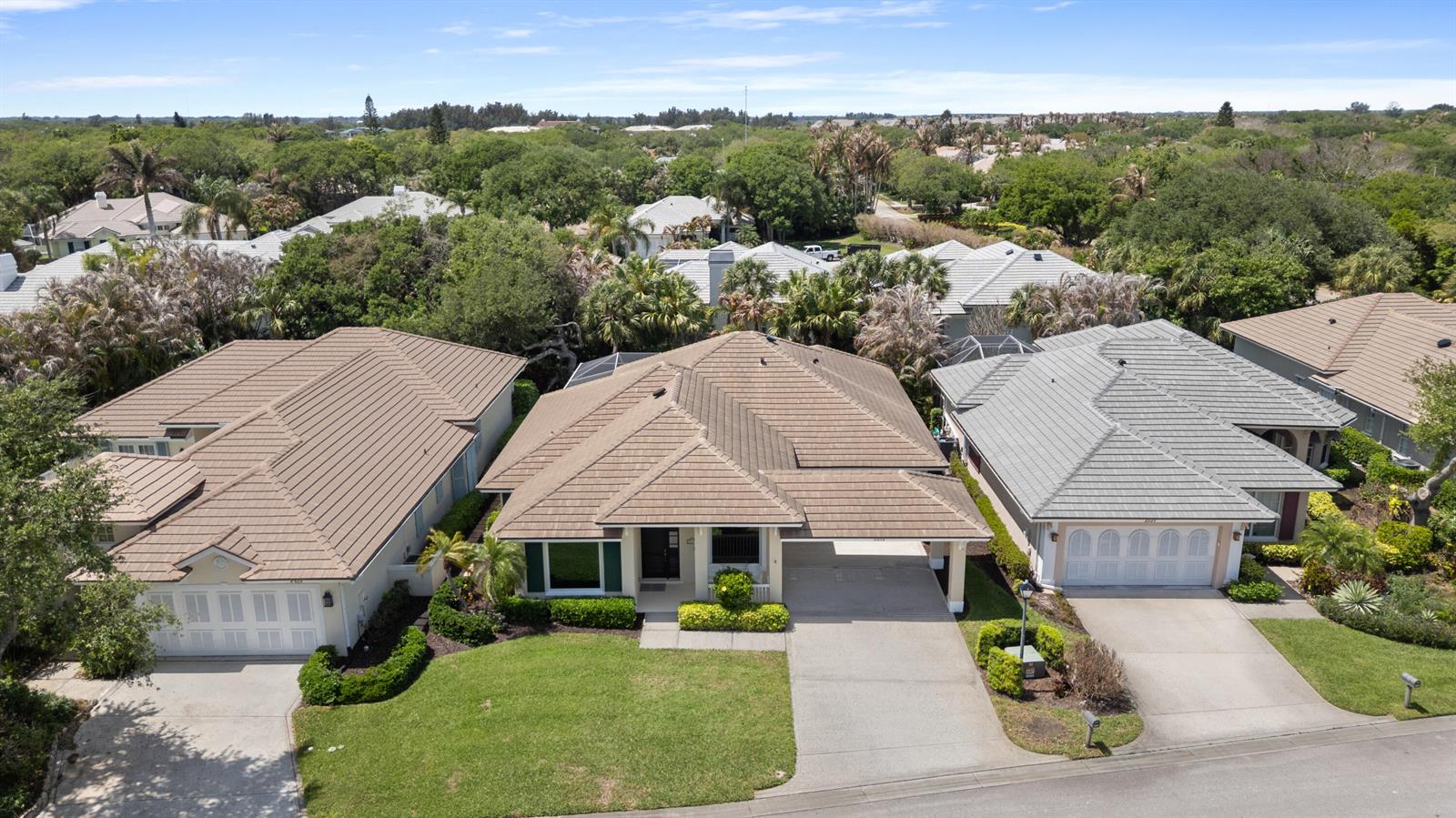 An aerial view shows three suburban houses with tiled roofs and driveways in a neighborhood — VERO BEACH, FL