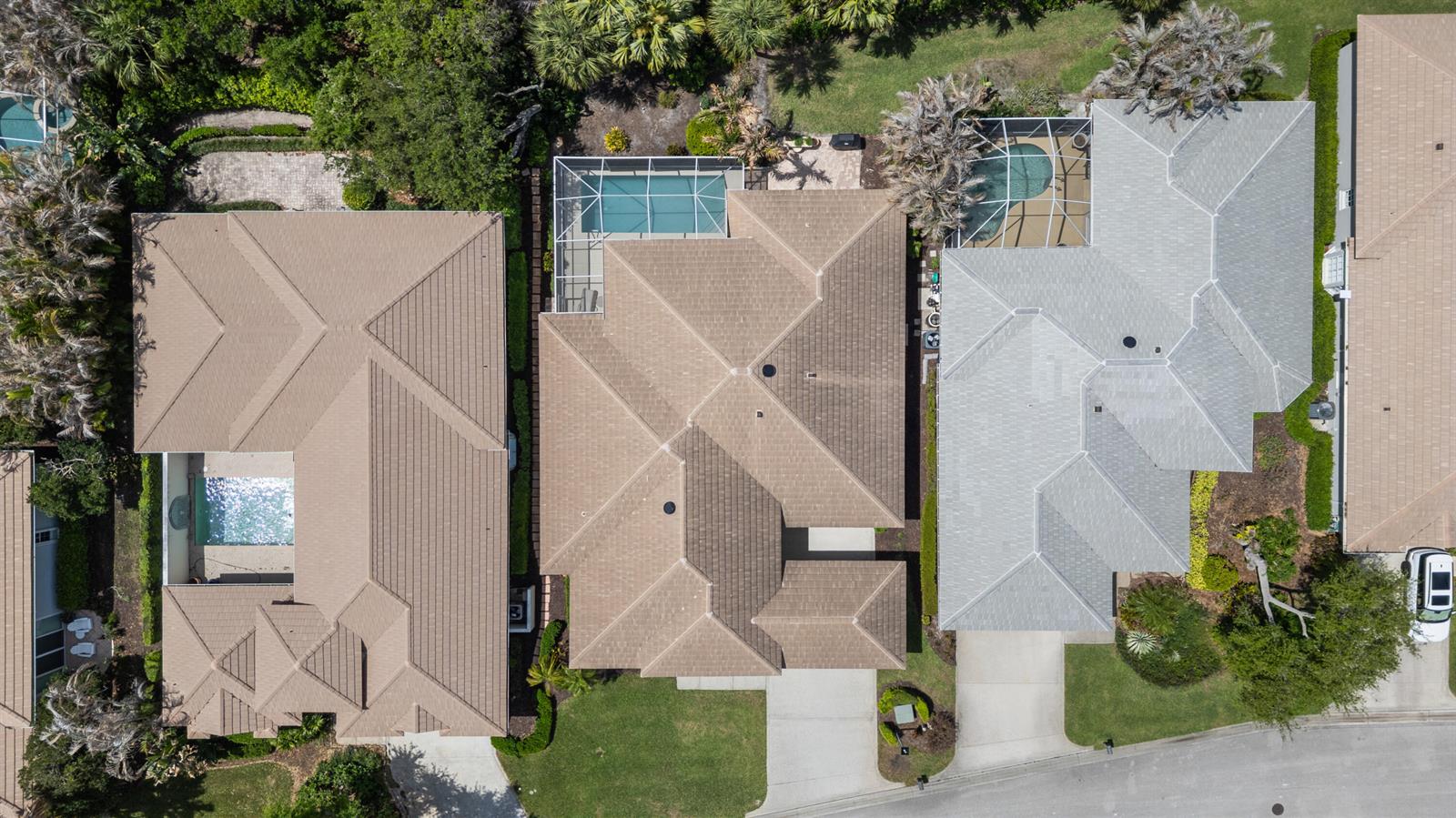 An aerial view shows three suburban houses with tiled roofs, swimming pools, and paved driveways — VERO BEACH, FL