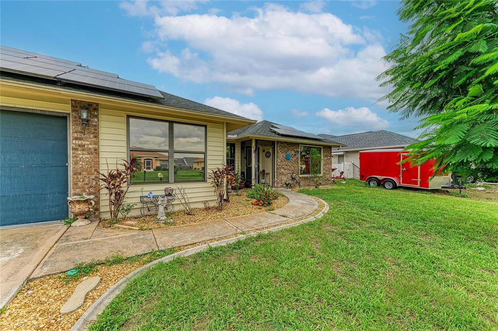 A single-story house with tan siding, brick accents, solar panels, and a red utility trailer — 2147 FLORIBANNA STREET, NORTH PORT, FL