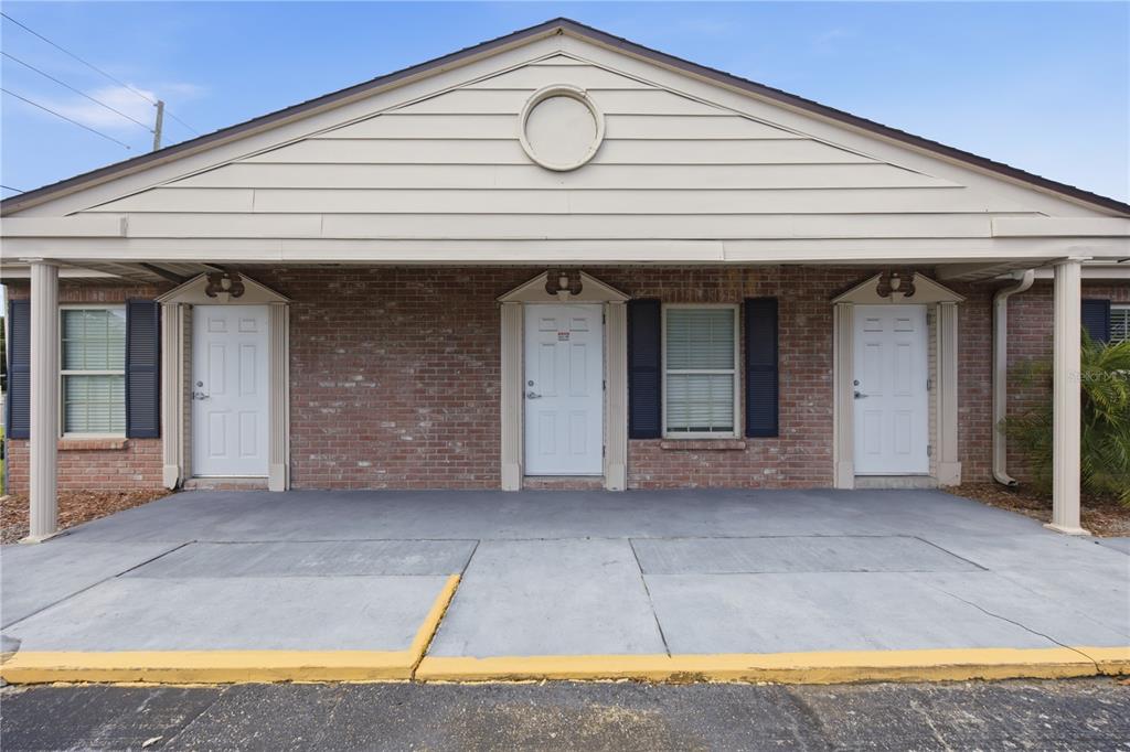 A brick building exterior features three white doors under a covered concrete walkway — 4911 STATE ROAD 54, NEW PORT RICHEY, FL
