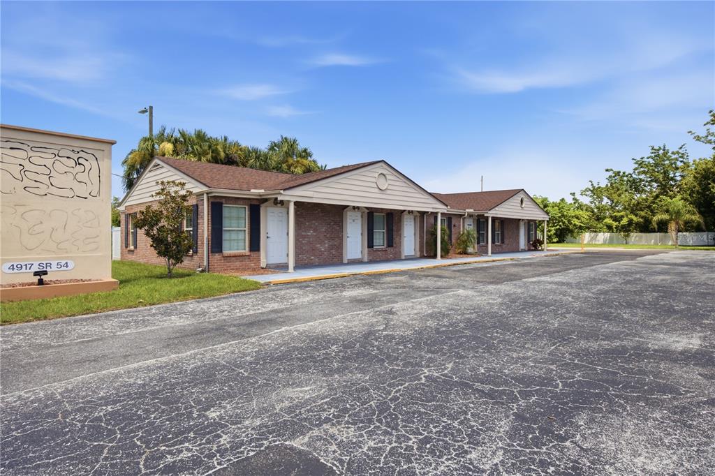 A single-story brick building with multiple entrance doors and a large asphalt parking lot — 4911 STATE ROAD 54, NEW PORT RICHEY, FL