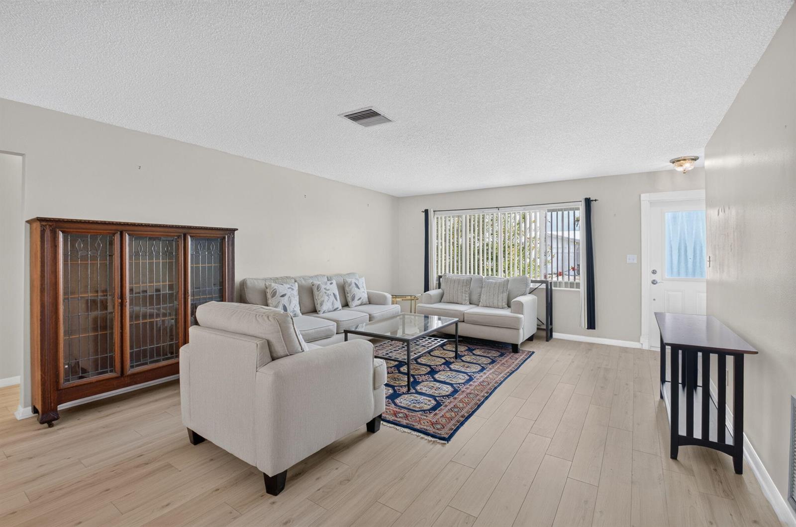A living room features light wood-look flooring, a patterned area rug, and neutral-toned seating furniture — 1710 SW 20th Street, Boynton Beach FL 33426, BOYNTON BEACH, FL