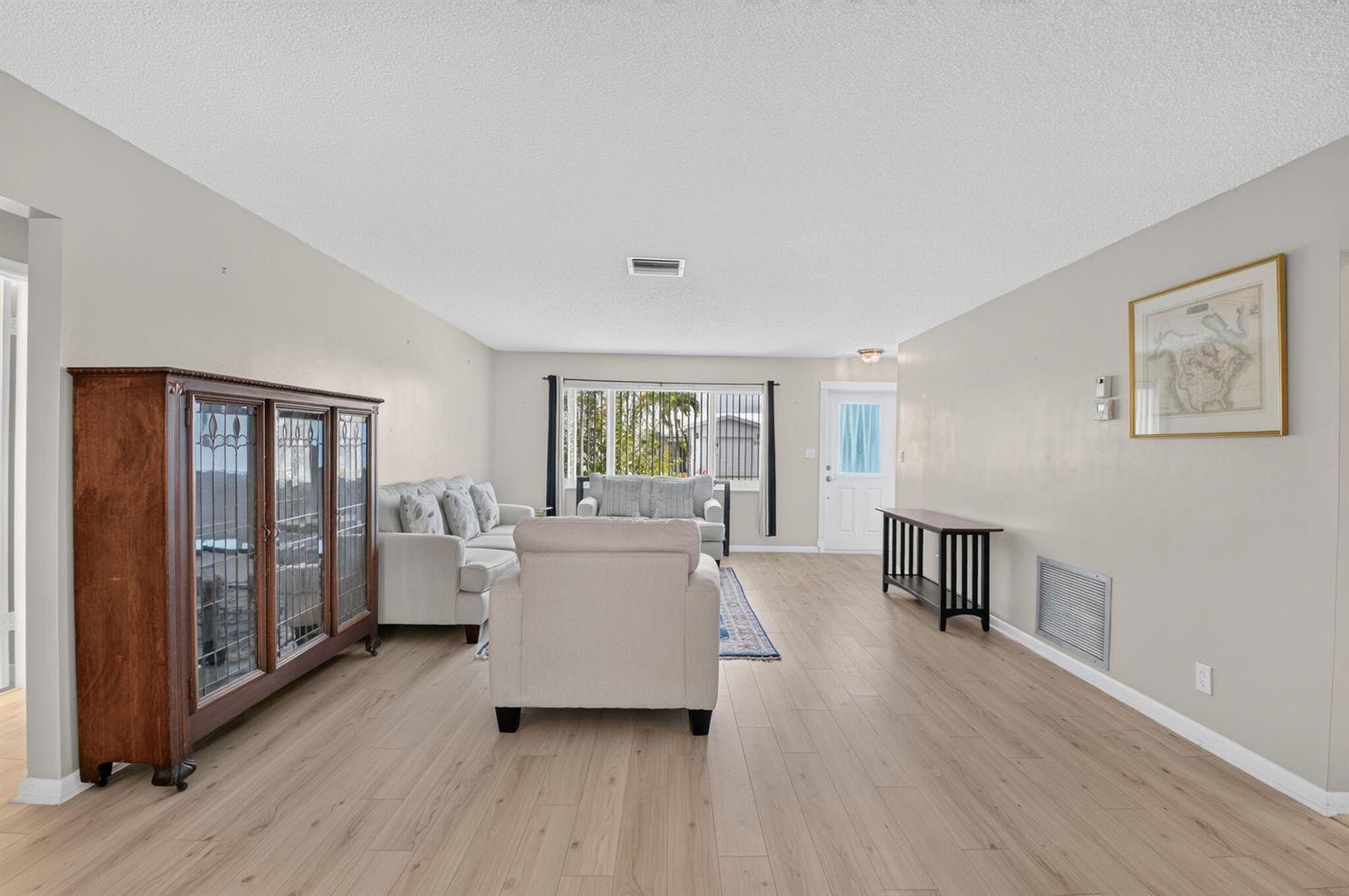 A living room with light wood flooring, neutral walls, a glass-front cabinet, and upholstered furniture — 1710 SW 20th Street, Boynton Beach FL 33426, BOYNTON BEACH, FL