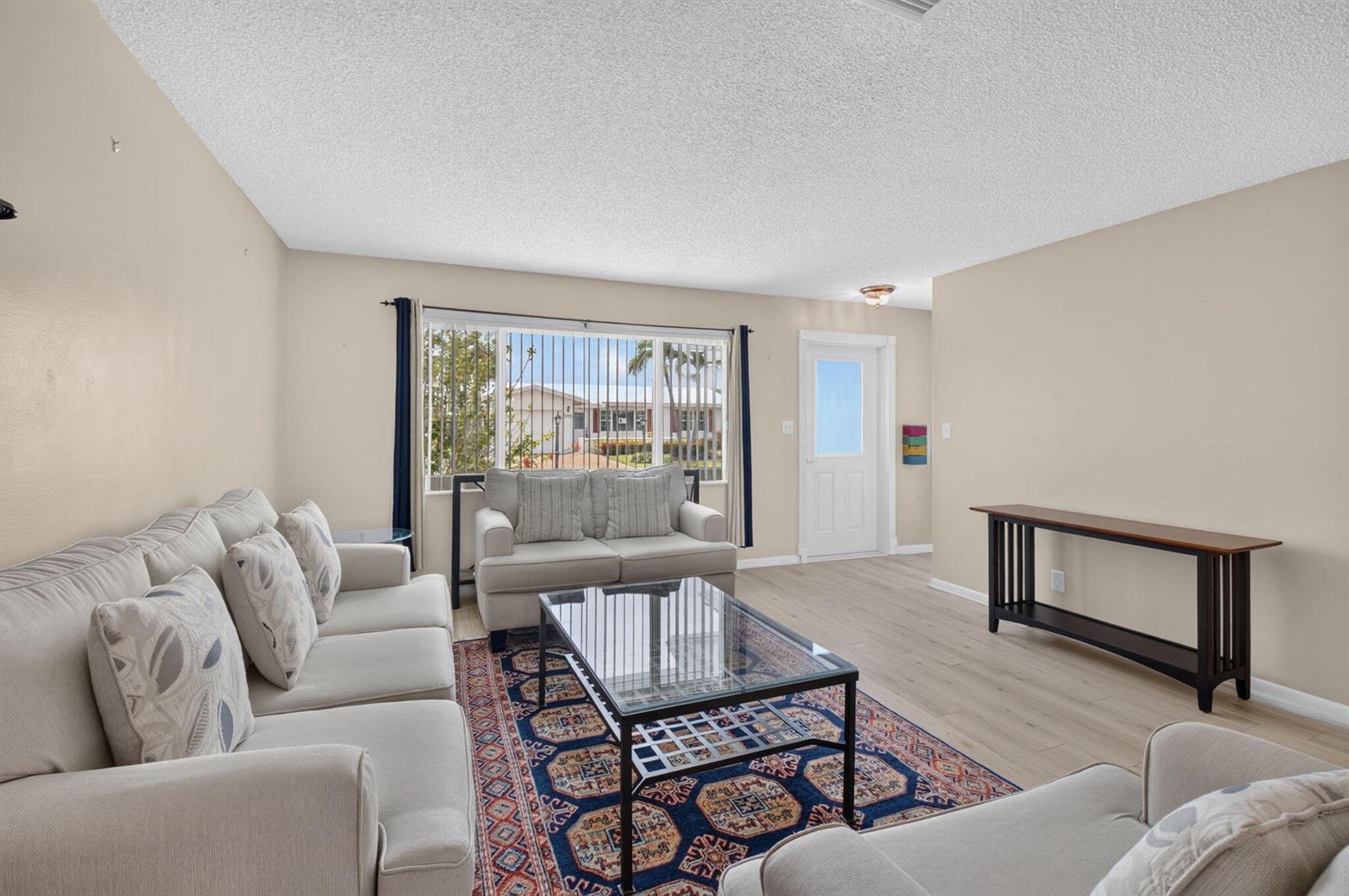 A living room features light-colored sofas, a glass coffee table, a patterned rug, and wood-look flooring — 1710 SW 20th Street, Boynton Beach FL 33426, BOYNTON BEACH, FL