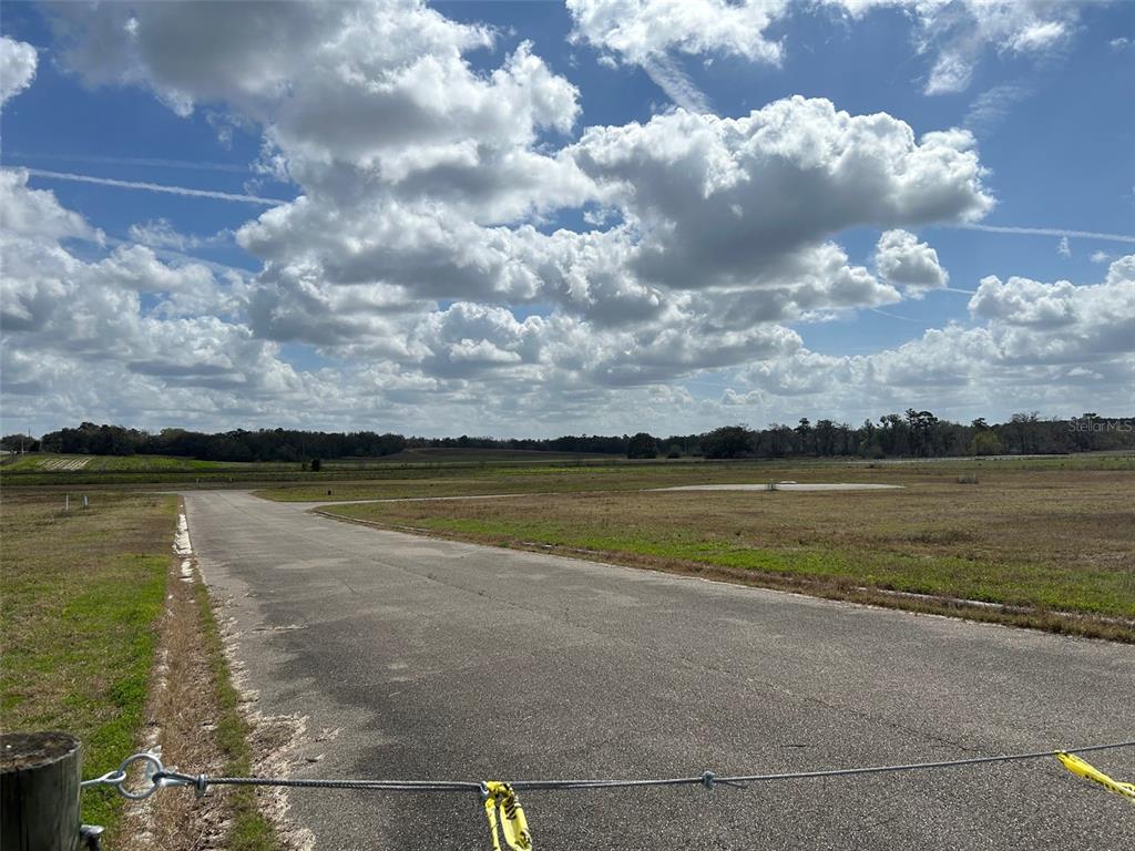 A paved road leads through an open, grassy field under a cloudy blue sky — NW US-441, ALACHUA, FL