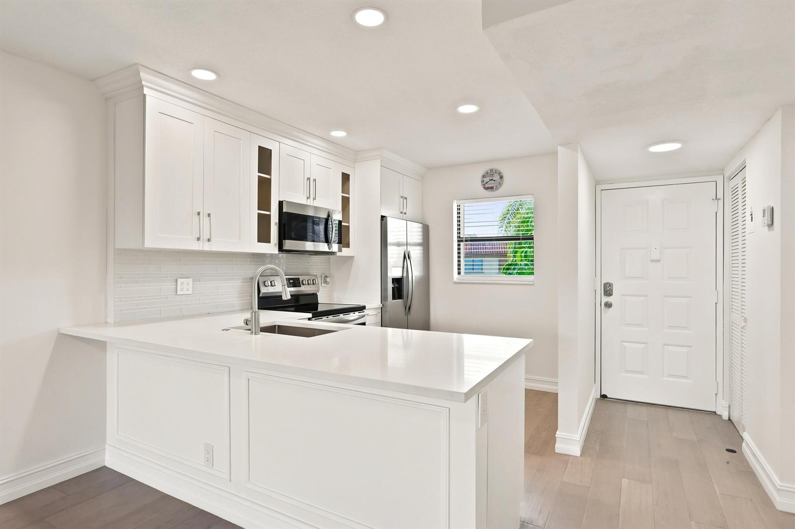 A modern kitchen features white cabinetry, quartz countertops, stainless steel appliances, and light wood flooring — 7209 Golf Colony Court # 203, Lake Worth FL 33467, LAKE WORTH, FL