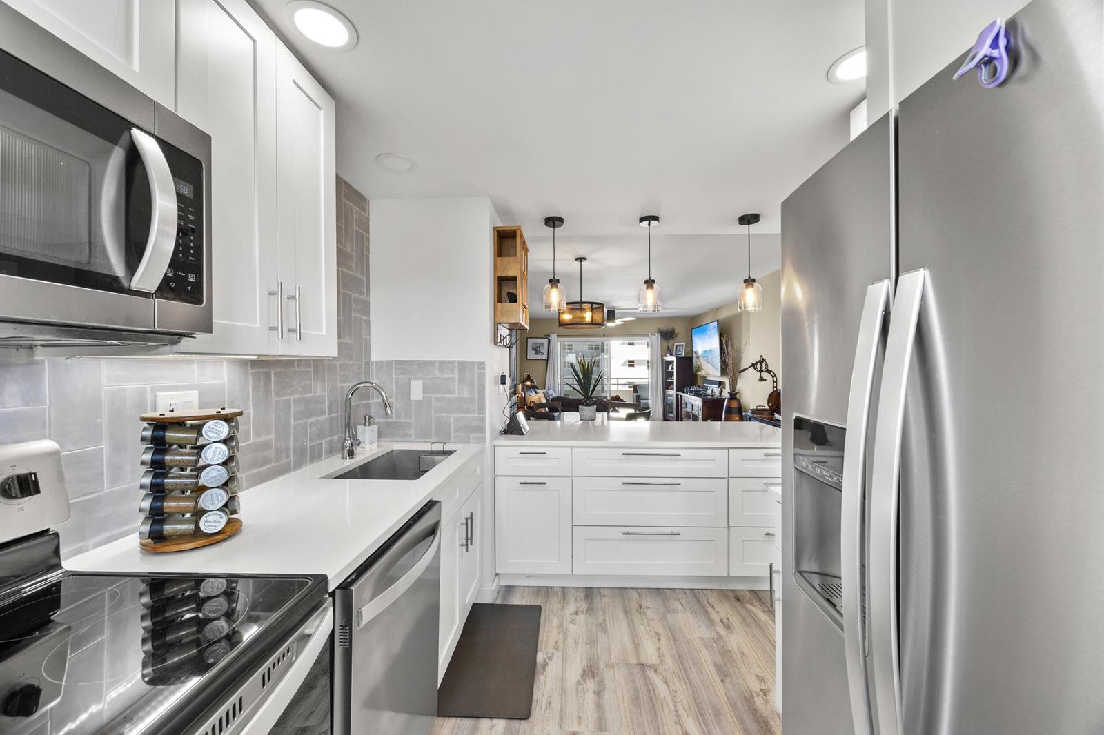 A modern kitchen features white cabinetry, stainless steel appliances, and a gray herringbone tile backsplash — 1630 N Ocean Boulevard # 812, Pompano Beach FL 33062, POMPANO BEACH, FL