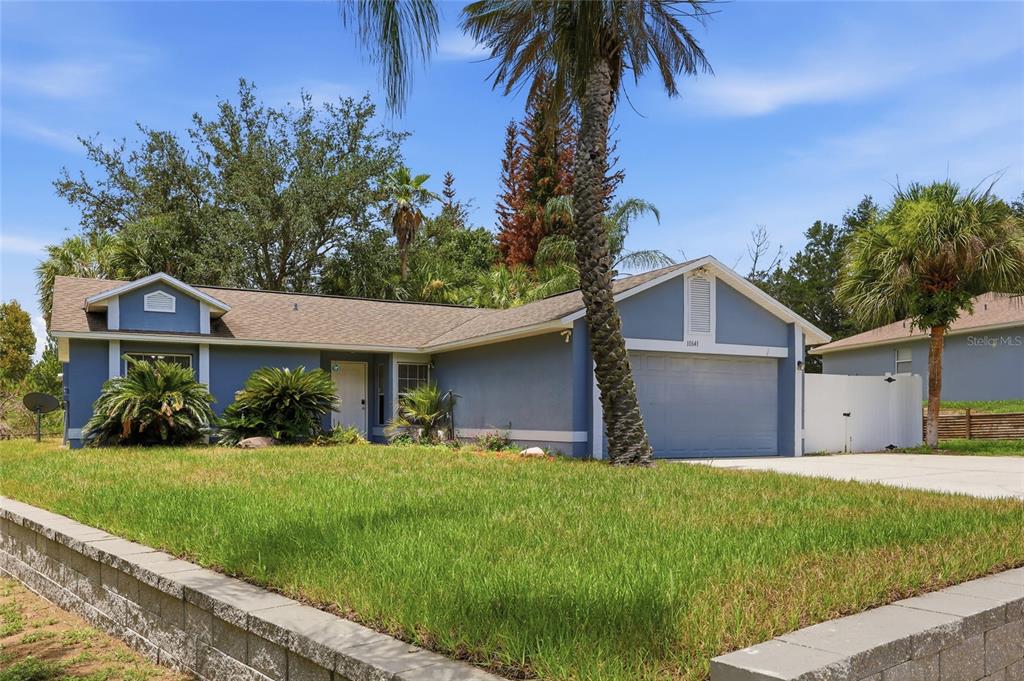 A blue single-story house with a two-car garage and a front lawn with palm trees — 10641 LAKE RALPH DRIVE, CLERMONT, FL