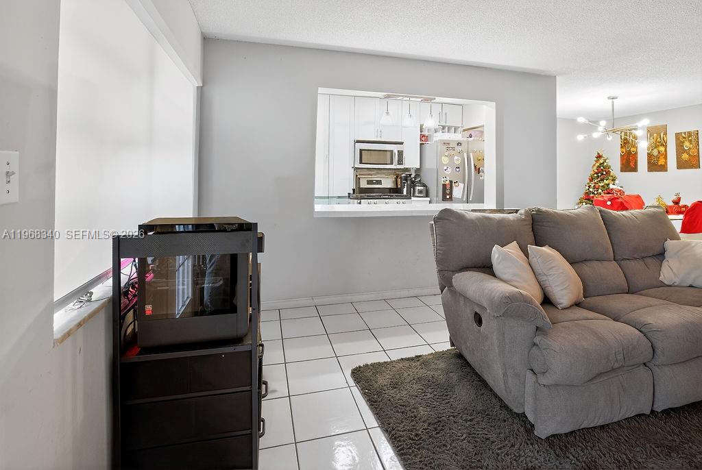 A living room features a gray sofa, a computer tower on a stand, and a kitchen pass-through — 20311 NE 2nd Ave # 15, Miami FL 33179, MIAMI, FL