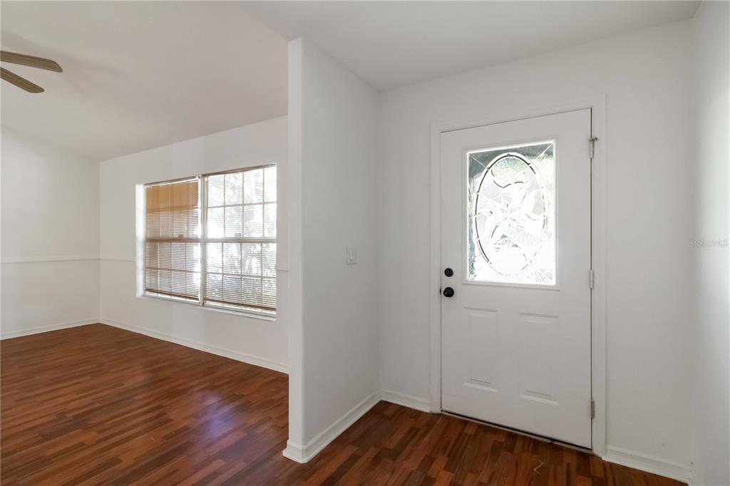 An entryway with wood-look flooring leads into a living room with white walls and windows — 6214 35TH AVENUE E, PALMETTO, FL