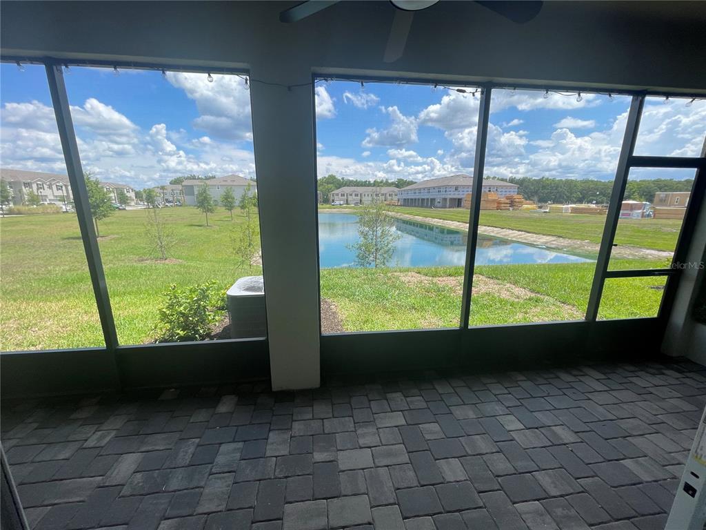 A screened-in patio with paver flooring overlooks a grassy lawn and a retention pond — 26068 WOVEN WICKER BEND, LUTZ, FL