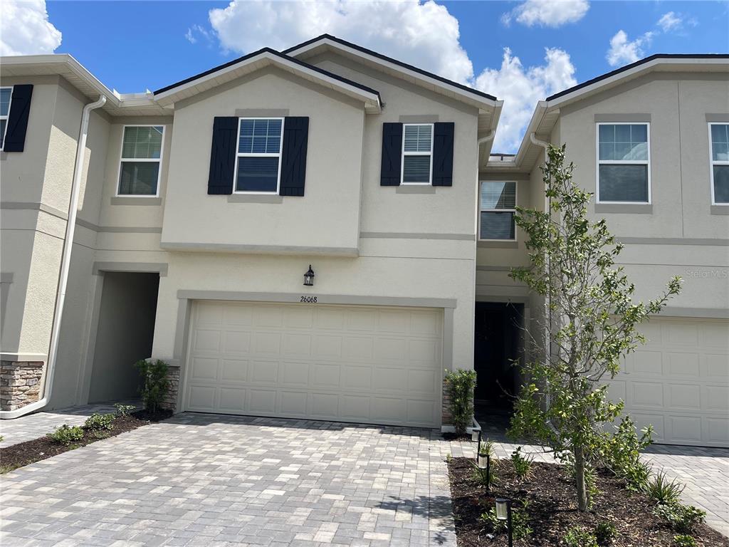A two-story townhouse exterior features a beige stucco facade, black shutters, and a paved driveway — 26068 WOVEN WICKER BEND, LUTZ, FL