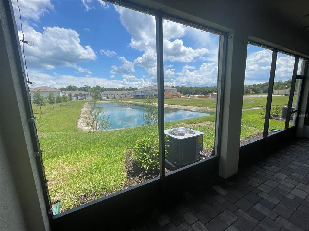 A view of a pond and construction site from a screened-in patio with pavers — 26068 WOVEN WICKER BEND, LUTZ, FL