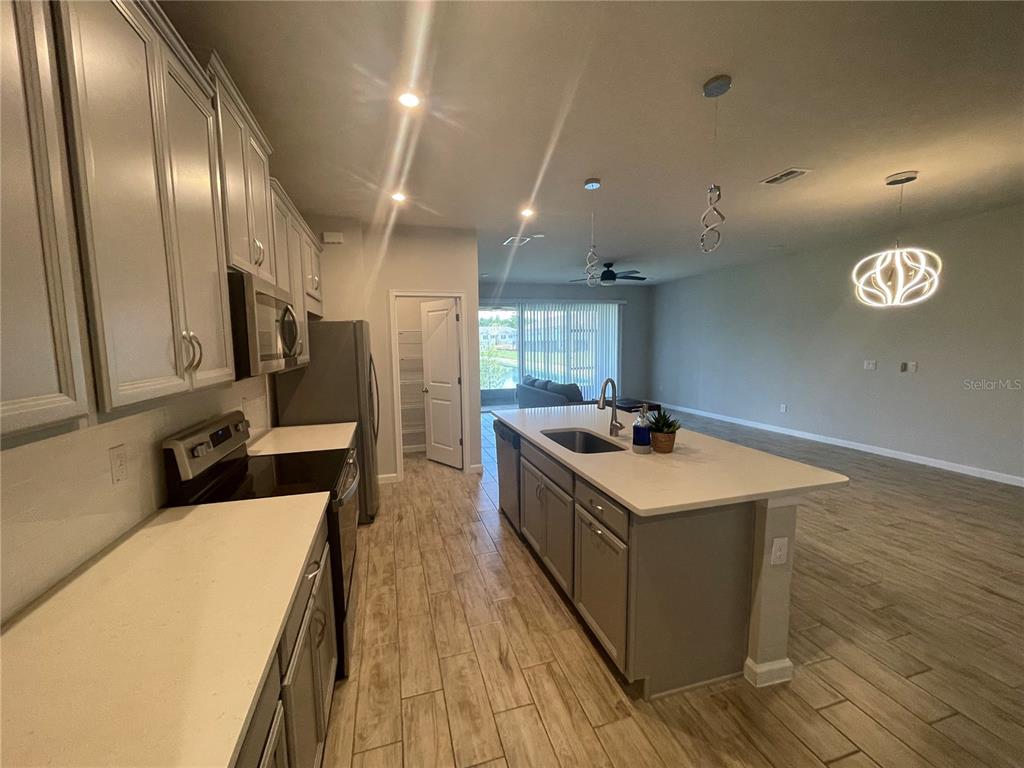 A kitchen with light gray cabinets, white countertops, and an island overlooks a living area — 26068 WOVEN WICKER BEND, LUTZ, FL