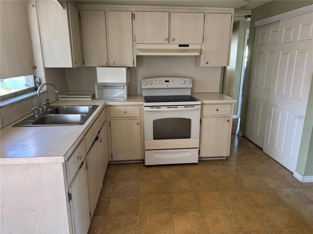 A kitchen features light wood cabinets, white appliances, a double sink, and vinyl flooring — 1321 HONOR DRIVE, HOLIDAY, FL