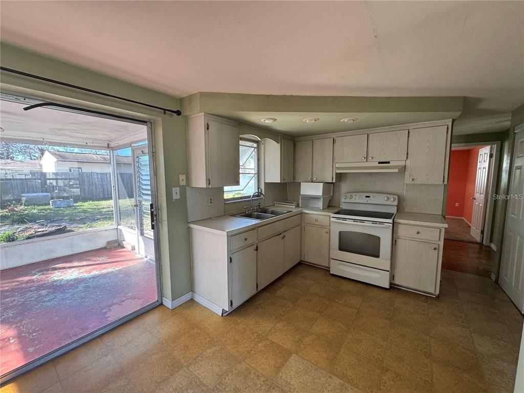 A kitchen with light-colored cabinets, white appliances, and a sliding glass door to a patio — 1321 HONOR DRIVE, HOLIDAY, FL