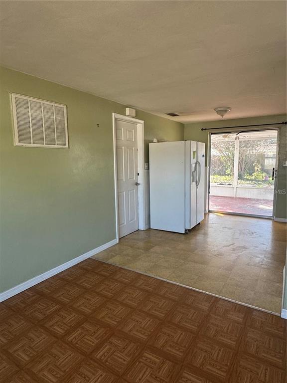 A room with parquet flooring, a white refrigerator, a closed door, and a sliding glass door — 1321 HONOR DRIVE, HOLIDAY, FL