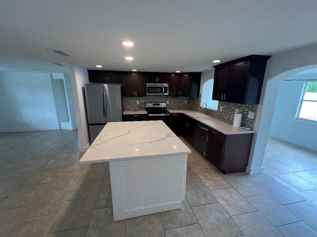 A kitchen features dark wood cabinets, a white marble-topped island, and light-colored tile flooring — 5270 CITADEL ROAD, VENICE, FL
