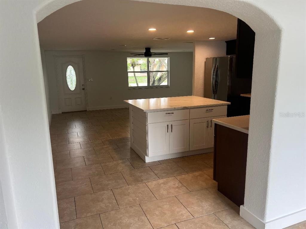 A kitchen with a white island and tile flooring is viewed through an arched doorway — 5270 CITADEL ROAD, VENICE, FL