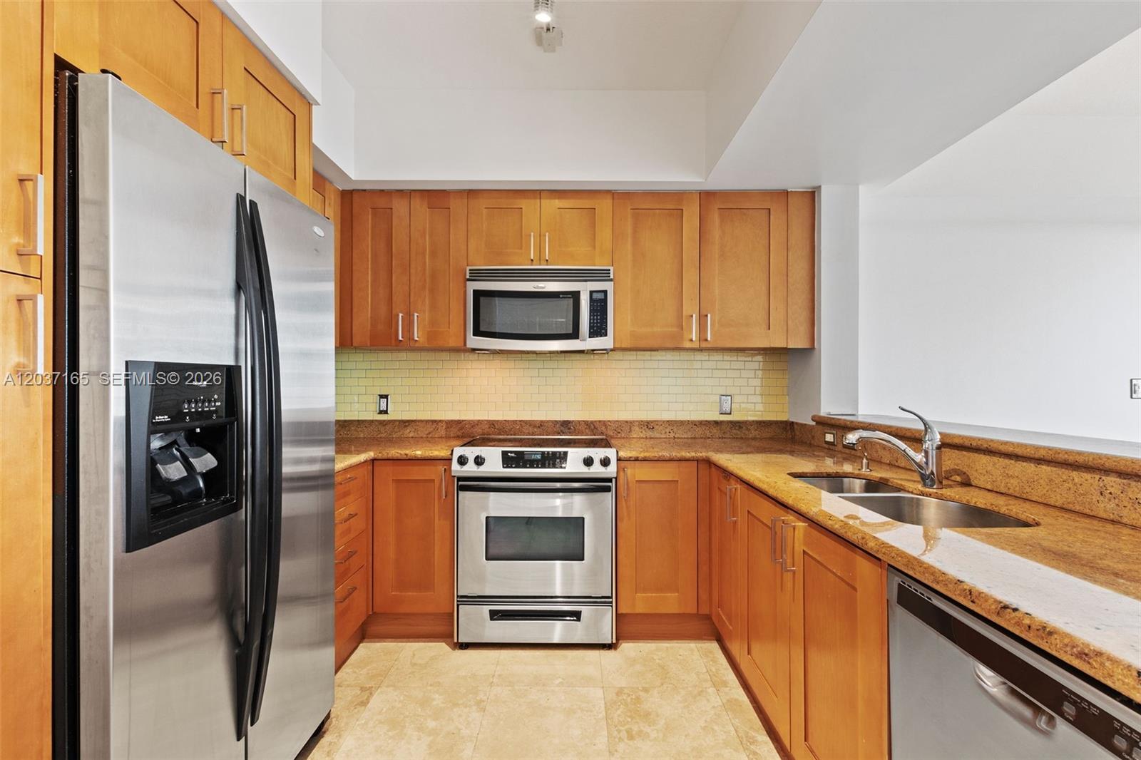 A kitchen features wood cabinets, stainless steel appliances, granite countertops, and a tile backsplash — 1755 E Hallandale Beach Blvd # 501E, Hallandale Beach FL 33009, HALLANDALE BEACH, FL