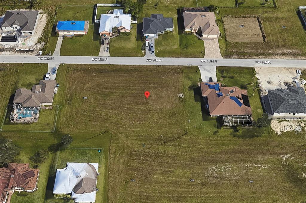 This aerial view shows a vacant residential lot situated between two houses on a street — 1012 NW 7TH PLACE, CAPE CORAL, FL