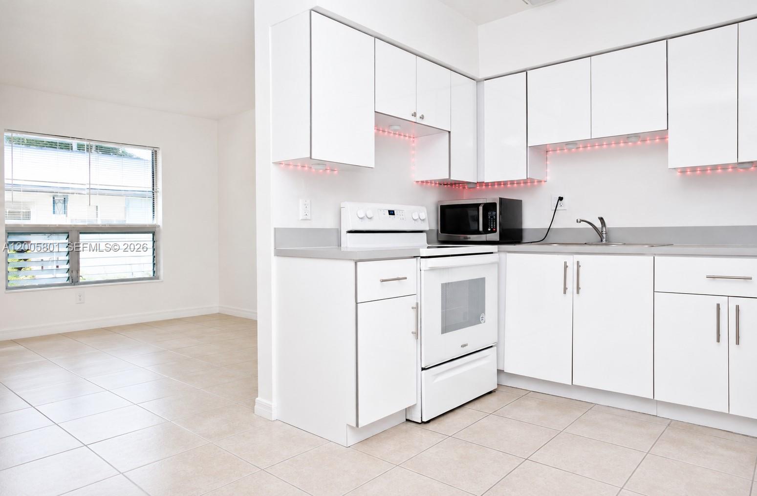A kitchen with white cabinets, a white stove, and a microwave next to a room — 2206 Fillmore St # 6, Hollywood FL 33020, HOLLYWOOD, FL