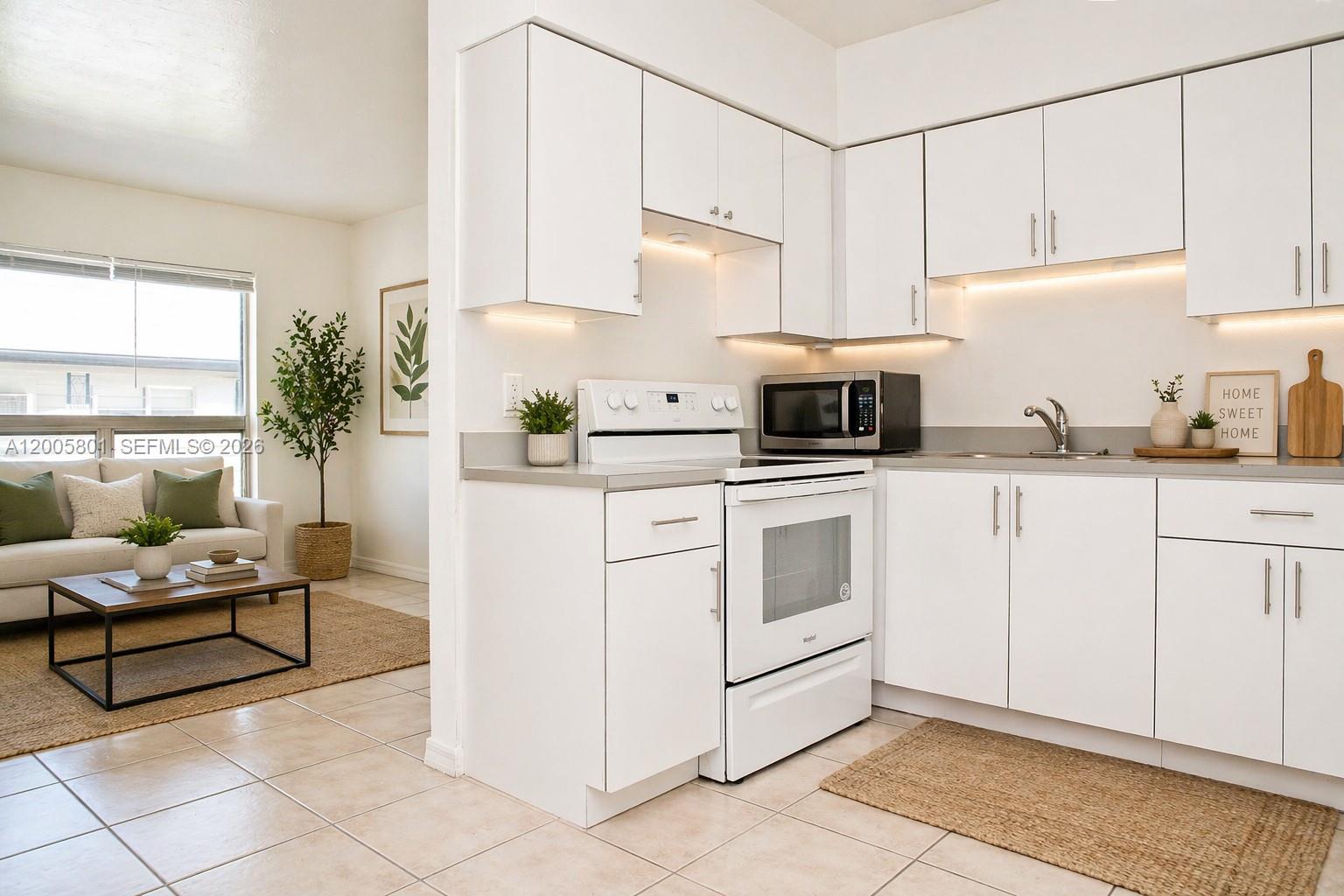 A white kitchen with a stove and microwave opens into a living area with tile floors — 2206 Fillmore St # 6, Hollywood FL 33020, HOLLYWOOD, FL