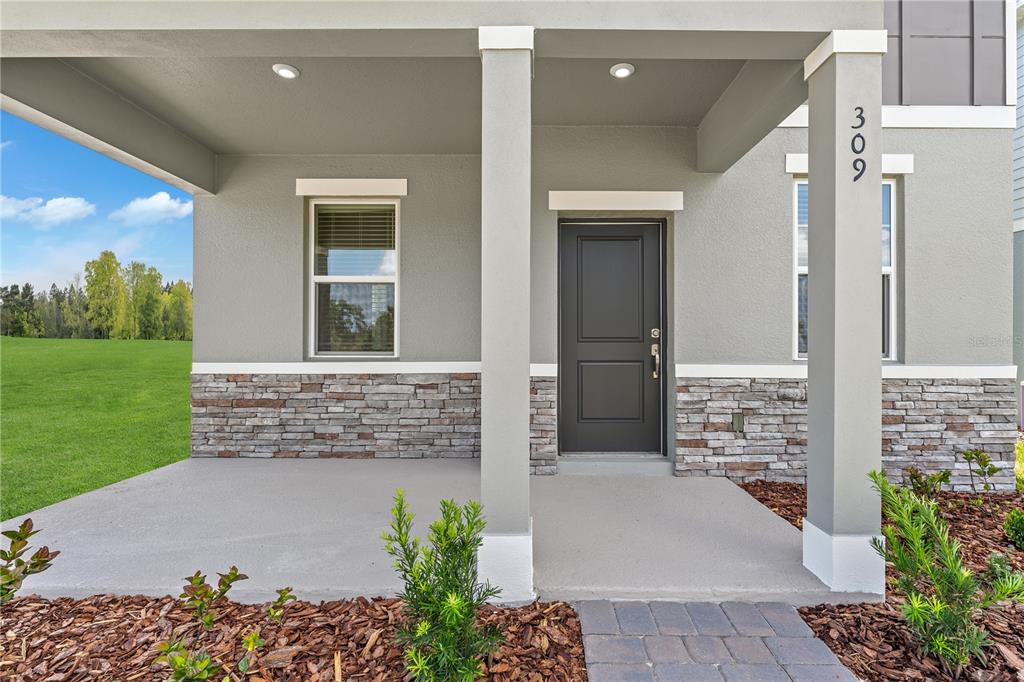 The exterior of a house features a covered porch, stone veneer, and a dark door — 4706 INNER WORLD LANE, WESLEY CHAPEL, FL