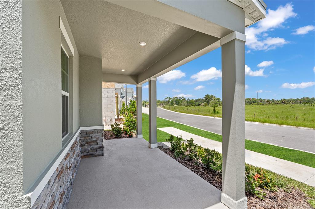 A covered front porch features stone veneer accents, square columns, and a concrete floor — 4706 INNER WORLD LANE, WESLEY CHAPEL, FL