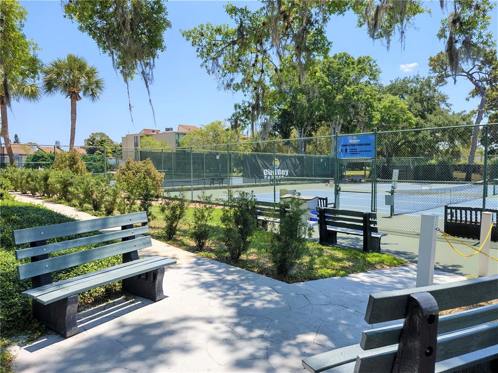 A tennis court with benches and landscaping is visible outdoors on a sunny day — 650 BIRD BAY DRIVE E UNIT 105, VENICE, FL