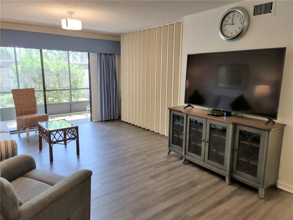 A living room features wood-look flooring, a large television on a console, and sliding glass doors — 650 BIRD BAY DRIVE E UNIT 105, VENICE, FL