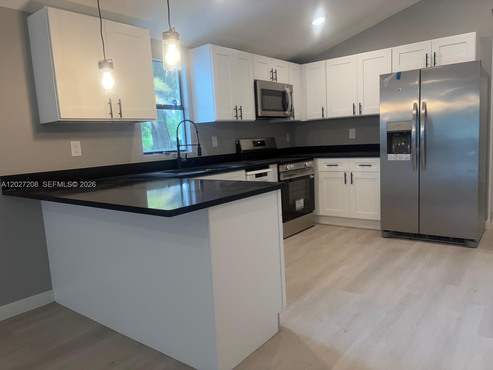 A modern kitchen features white cabinets, black countertops, stainless steel appliances, and light wood flooring — 2331 Randall St, Sanford FL 32771, SANFORD, FL