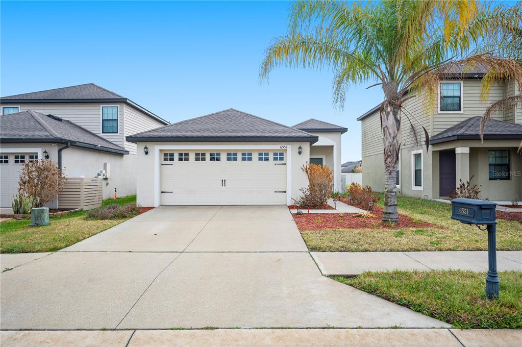 A single-story house with a two-car garage and a palm tree in the front yard — 6551 BAIKAL PLACE, LAKELAND, FL