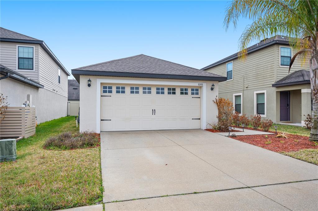 A beige detached garage with a concrete driveway sits between two houses under a blue sky — 6551 BAIKAL PLACE, LAKELAND, FL