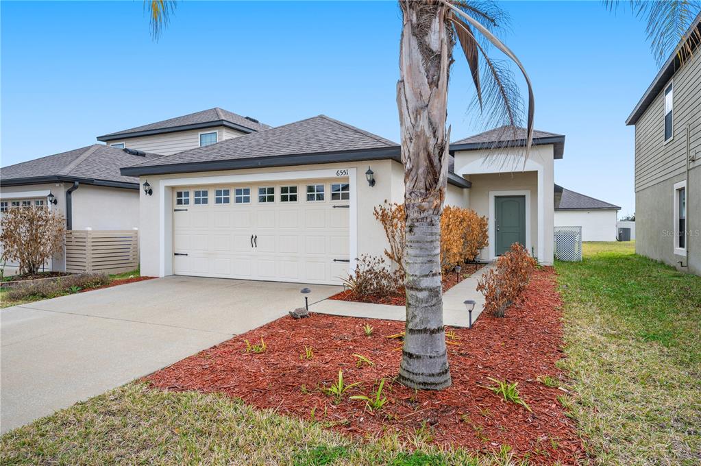 A single-story house with a beige exterior, a two-car garage, and a palm tree — 6551 BAIKAL PLACE, LAKELAND, FL